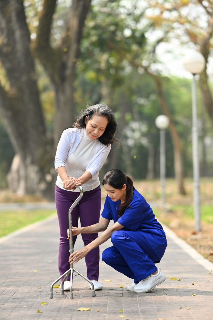 Attentive practitioner nurse assisting senior female walking with tripod cane. Assistance, rehabilitation and health.