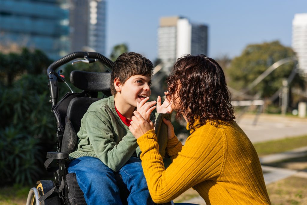 Happy child in wheelchair playing with mother outdoors
