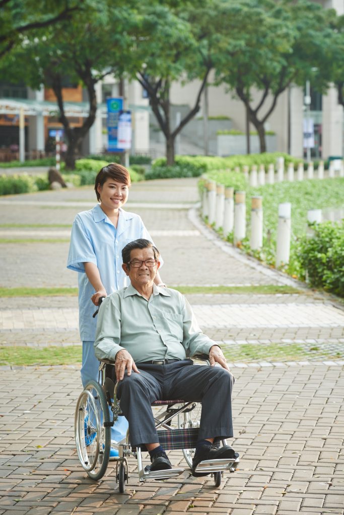 Smiling nurse walking in park with senior patient in wheelchair
