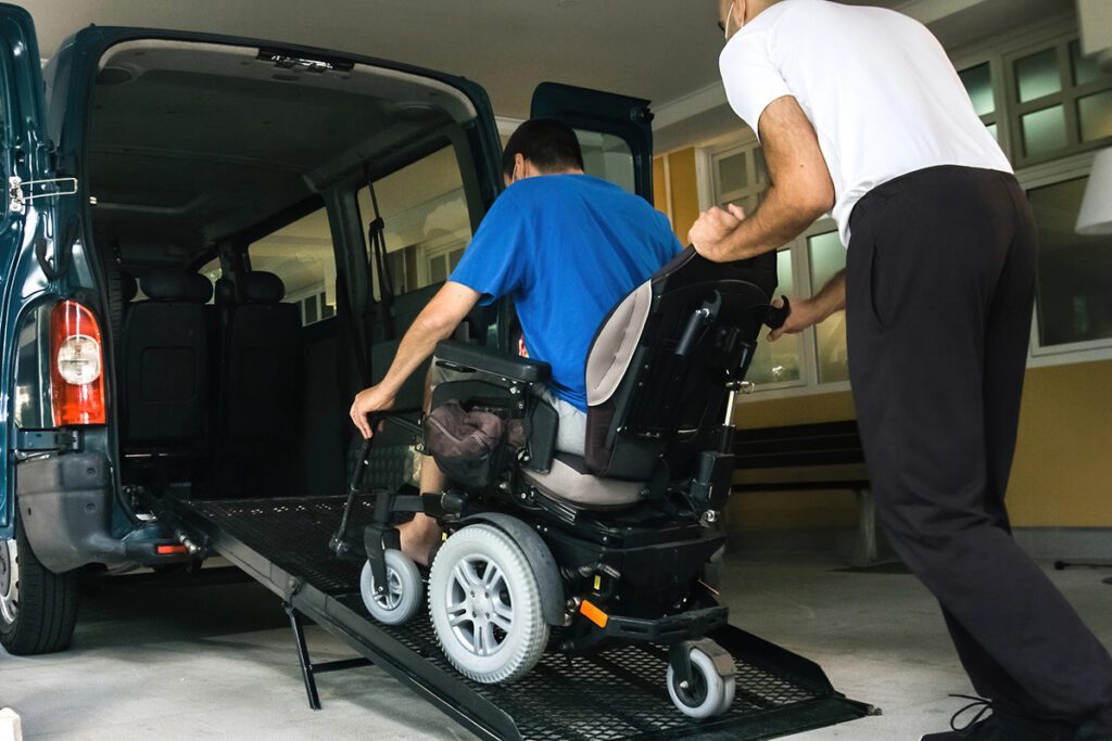 Support worker assisting NDIS participant into accessible transport vehicle.
